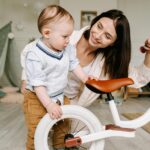 Mother and young child interact with a bicycle indoors, sharing joy and bonding.
